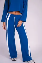 Pantalón deportivo azul de corte holgado y pierna ancha, con cintura elástica, cordón ajustable blanco y franjas laterales blancas.