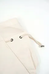 Bolso tipo tote bag color beige con asas superiores de hombro, cordones ajustables a los lados con detalles metálicos y un pequeño anillo frontal.