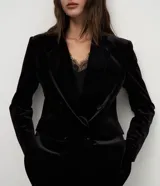 Blazer de terciopelo color negro con largo extendido, diseño cruzado con botones frontales, solapa clásica, bolsillos con tapa y mangas largas.