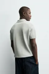 Jersey de punto color verde oliva, de calce relajado (relaxed fit), con cuello solapa y abertura frontal en forma de V. Es de manga corta y presenta acabados en rib en puños y ruedo.