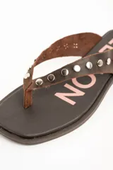 Sandalias planas de cuero marrón tipo ojota con tiras anchas adornadas con tachas metálicas plateadas y plantilla con diseño estampado.