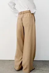 Pantalón recto color beige de tiro medio, con cintura elástica, bolsillos delanteros y cinturón ajustable con hebilla metálica dorada.