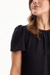Blusa de manga corta con pliegues en escote redondo, confeccionada en tela crepé de color beige.