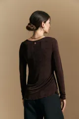 Top de manga larga con textura suave y leve brillo. Presenta una silueta al cuerpo, tajos laterales y terminaciones onduladas en el ruedo.