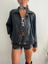 Campera negra de cuero sintético con costuras blancas a contraste, cierre con botones metálicos y cuello clásico.