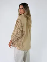 Camisa blanca con cuello camisero, cierre frontal de botones y mangas tres cuartos abullonadas con bordados suizos y detalles perforados en los laterales y mangas.