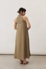Vestido largo color marrón, sin mangas y con escote halter. Cuenta con bolsillos laterales y corte holgado.