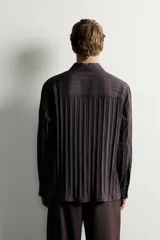 Camisa de manga larga con ajuste relajado, confeccionada en tejido de viscosa con textura de rayas verticales. Presenta cuello camisero, cierre frontal de botones y aberturas en el bajo lateral.