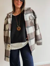 Sobrecamisa de paño con diseño a cuadros en tonos marrones, grises y blancos. Presenta cuello clásico, cierre frontal con botones y bolsillos delanteros con tapa.
