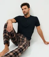 Pijama masculino compuesto por una remera negra de manga corta con cuello henley y botones, y un pantalón largo con estampado de cuadros en tonos marrones, negros y blancos.