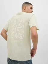 Camiseta color arena con estampado en la espalda con la palabra 'ORIGINALS' y un diseño abstracto en blanco.