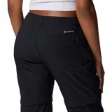 Pantalón técnico convertible en short, color negro, con diseño funcional para actividades al aire libre. Presenta rodillas articuladas, múltiples bolsillos incluyendo uno de seguridad con cierre, presillas para cinturón y dobladillo ajustable. Las piernas son desmontables mediante cierres diferenciados.