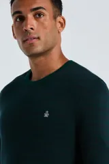 Sweater de punto color verde oscuro, con cuello redondo, mangas largas y puños acanalados. Presenta el logo de la marca bordado en el pecho.