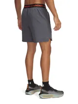 Short deportivo Under Armour Vanish Woven de color gris, diseñado para entrenamientos intensos. Presenta un tejido ultraligero y transpirable con paneles de malla estratégicos, cintura elástica con detalle de marca en la parte trasera y bolsillos laterales abiertos. Incluye el logo de la marca en color naranja en la pierna derecha.