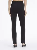 Pantalón negro de punto técnico, corte slim, pierna acampanada con aberturas traseras, talle medio, cierre de cremallera oculto y detalles de costuras verticales.