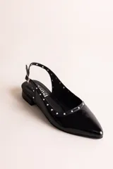 Chatitas destalonadas de cuero charolado color beige con punta fina, taco bajo y detalle de tachas metálicas doradas alrededor del borde.