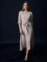 Vestido maxi color beige, con cuello mao y escote en V. Presenta mangas largas con presilla y botón para regular el largo, y un lazo ajustable en la cintura que marca la silueta.