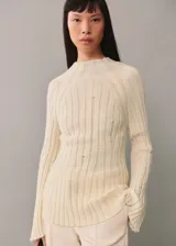 Buzo de punto acanalado color crema con diseño desagujado, cuello perkins y mangas largas acampanadas.