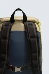 Mochila confeccionada en tejido técnico con bloques de color beige, amarillo y verde, y detalles en piel. Cuenta con un compartimento principal con cierre de solapa, hebilla y cordón ajustable, bolsillos laterales planos y correas de hombro regulables con hebilla de liberación rápida.