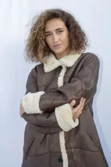 Campera tipo gamulán de cuero genuino en color marrón, con interior y detalles en corderito sintético color crema. Presenta cierre frontal con botones, cuello solapa y puños con vuelta.