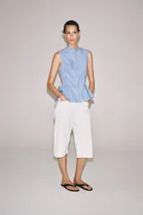 Camisa sin mangas de algodón con rayas verticales blancas y azules, cuello mao, bajo acabado en peplum y cierre frontal con alamares decorativos de nudo.