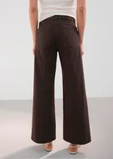 Jeans de corte wide leg y tiro medio color marrón oscuro, con bolsillos delanteros aplicados de estilo cargo y cierre frontal con botón y cremallera.