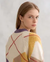 Cárdigan tejido de punto con diseño de rombos, en colores crema, violeta y detalles en rojo. Presenta cuello redondo, cierre frontal con botones de madera y textura acanalada en los bordes.