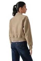 Campera tipo bomber de corte cropped, confeccionada en microgamuza color tostado. Presenta cierre frontal con botones a presión metálicos, cuello redondo y puños elásticos acanalados.