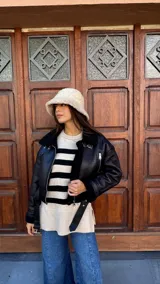 Campera tipo gamulán de cuero sintético negro con interior de corderito sintético al tono. Presenta cuello solapa, cierre frontal con cremallera metálica, correas ajustables con hebillas en el cuello y en el ruedo, y mangas largas.
