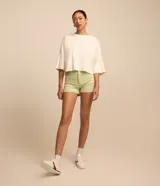 Short de sarga color blanco, de cintura alta, con bolsillos delanteros y traseros, trabillas para cinturón y bajo plegado. Cuenta con cierre frontal de botón y cremallera.