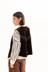 Chaleco oversize confeccionado en cuero descarne, con diseño de terminación en picos y cierre frontal con lazos y ojalillos. Presenta tachas metálicas decorativas en los hombros y en la parte posterior.