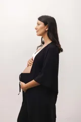 Conjunto de ropa de descanso para maternidad compuesto por un pantalón negro de tiro alto y corte ancho con cordón ajustable, un top de lactancia blanco con escote en V y una bata negra de manga ancha con lazo para atar.