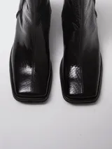 Bota de caña media con punta cuadrada y cierre lateral, confeccionada en cuero con textura croco y acabado charol negro.