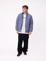 Campera reversible de nylon con cuello alto y cierre frontal. Un lado es de color gris liso con logo bordado, mientras que el otro lado presenta un estampado abstracto en tonos azules. Cuenta con bolsillos laterales y puños elásticos.