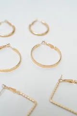 Set de siete pares de aros dorados de diversos diseños, incluyendo aros tipo argolla redondos en dos tamaños, aros cuadrados con textura y varios modelos de aros pequeños tipo broquel con detalles de piedras y esferas.