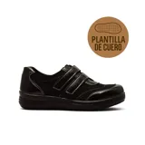Zapato casual de mujer color negro, con cierre de doble velcro y combinación de texturas en cuero y charol. Cuenta con suela plana de goma y plantilla de cuero.