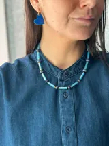 Collar corto de diseño artesanal compuesto por cuentas cilíndricas de vidrio en tono celeste y pequeñas piedras naturales esféricas en tonos azulados, intercaladas con detalles metálicos. Incluye cadena de acero quirúrgico para ajuste de largo.