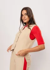 Chaleco beige con escote en V, sin mangas y cierre frontal con botones. Presenta pespuntes en color rojo y logo bordado en la espalda.