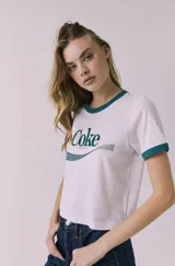 Remera de manga corta estilo ringer, color blanca con ribetes verde oscuro en cuello y puños. Cuenta con estampado frontal de Coca-Cola en color verde.