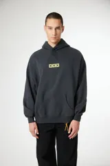 Hoodie gris oscuro con capucha, bolsillo canguro frontal y un pequeño gráfico bordado en amarillo con tres 'X' en el pecho.