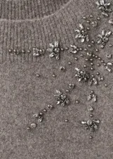 Jersey de punto grueso en color gris, con cuello barco que deja un hombro al descubierto, manga larga y diseño recto. Presenta un detalle de cristales bordados en la parte superior delantera.