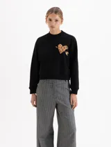 Buzo negro de corte regular, confeccionado en rústico de algodón con cuello redondo, puños y cintura en ribb. Presenta una estampa frontal de un corazón con diseño de animal print atravesado por una flecha.
