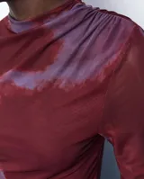 Vestido midi de microtul con diseño drapeado lateral, cuello alto y mangas largas. Presenta un estampado tipo tie-dye en tonos bordó y violeta.