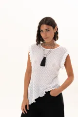 Blusa de textura rugosa en color blanco, sin mangas, con detalle de volados en los hombros y corte asimétrico en el ruedo.