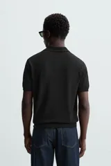 Polo de punto negro, manga corta, con cuello solapa y cierre frontal de tres botones. Presenta un calce regular y acabados en rib en mangas y ruedo.