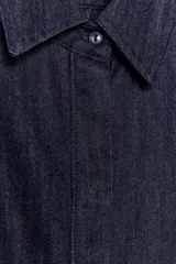 Camisa de denim azul oscuro con cuello solapa, manga larga con puños y diseño peplum en el bajo. Presenta cierre frontal con botones ocultos por solapa.