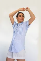 Camisa de manga corta con combinación de patrones a rayas y cuadros en tonos celeste y blanco, con bolsillo frontal aplicado y cierre de botones.