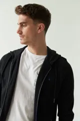 Campera con capucha de felpa color negro, con cierre frontal y puños. Presenta un pequeño logo bordado en azul en el pecho.