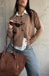 Cardigan de punto trenzado en color beige, con cuello redondo, cierre frontal de botones oscuros y mangas largas con puños acanalados.