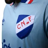 Camiseta de fútbol Umbro del Club Nacional de Football, tercera equipación modelo Away 3. Diseño en color celeste con cuello polo y puños en azul, blanco y rojo. Incluye logo de Umbro, escudo del club y el sponsor Antel en el frente.
